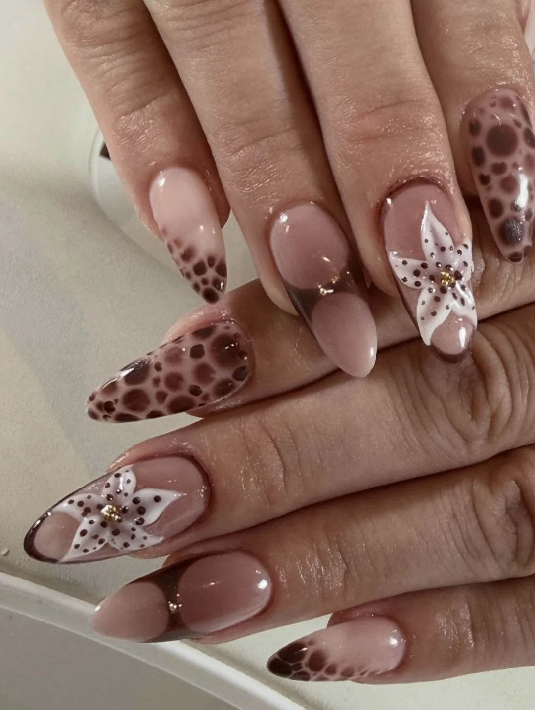 Ongles amande nude avec lys blancs mouchetés, french chocolat et motif tacheté
